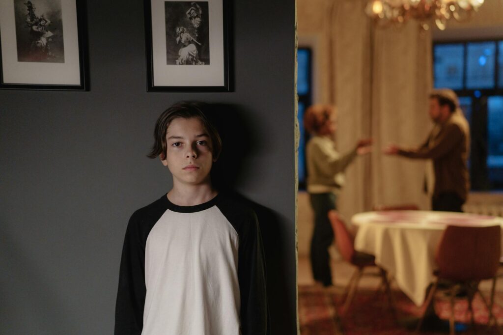 O que configura alienação parental - Robison Souza - Perito em Psicologia Forense A boy stands in focus, while two adults argue in the background, depicting family conflict.