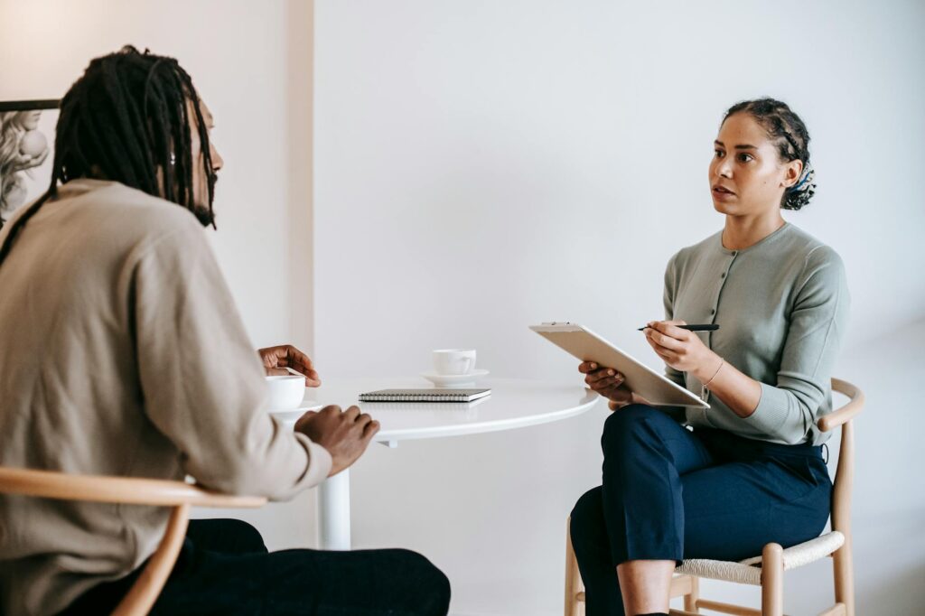 O que é perícia psicológica forense - Robison Souza - Perito em Psicologia Forense Focused ethnic female interviewer or psychotherapist asking questions and writing notes in clipboard while looking at African American male