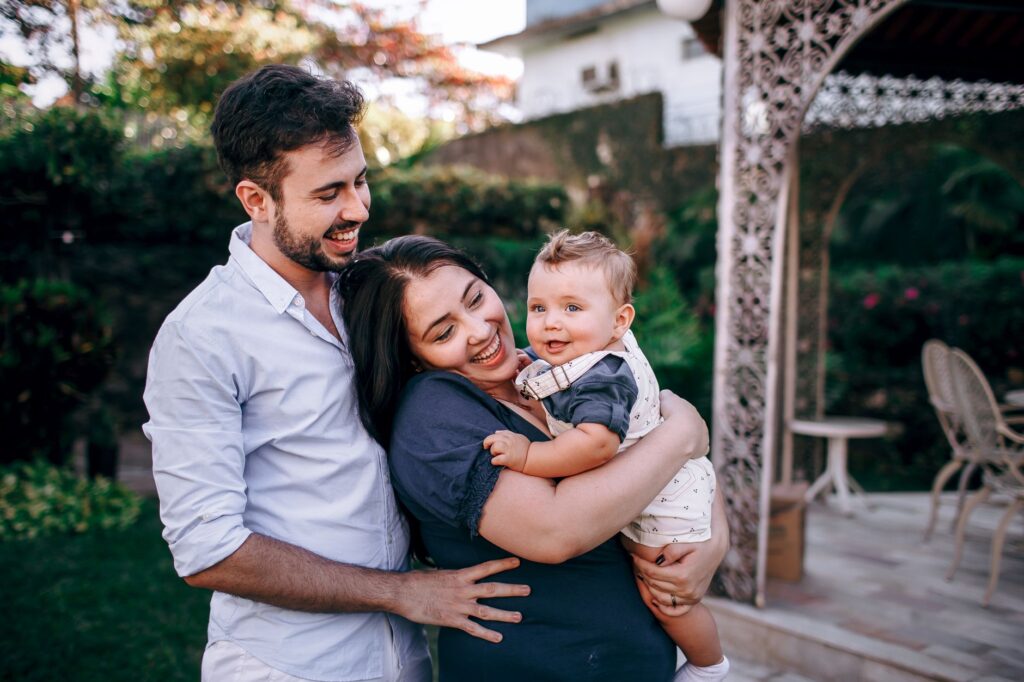 Como processar por alienação parental - Robison Souza - Perito em Psicologia Forense A joyful family moment outdoors with parents and baby in a garden setting.