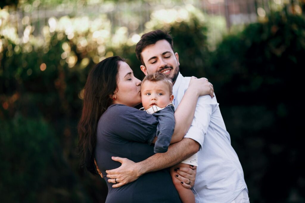 O que é alienação parental resumo - Robison Souza - Perito em Psicologia Forense A family of three shares a warm, loving hug outdoors surrounded by lush greenery.