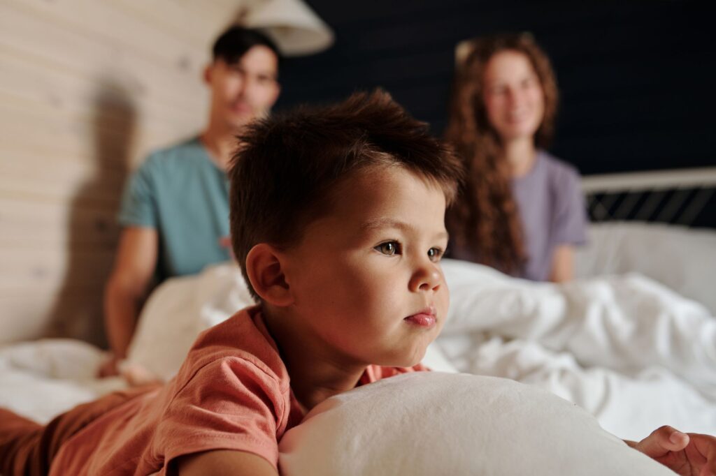 O que é síndrome de alienação parental - Robison Souza - Perito em Psicologia Forense Adorable child lying on bed with parents in cozy indoor setting, showcasing family warmth.